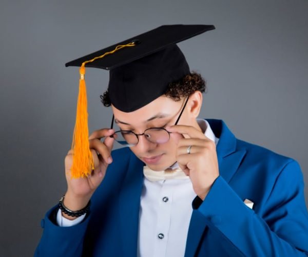 Portrait of a young man in a graduation cap adjusting glasses, celebrating achievement.